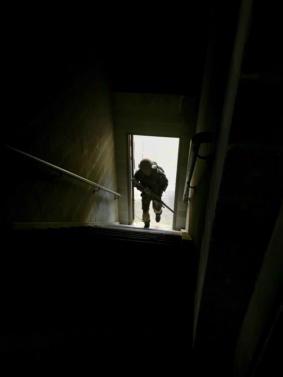 A sniper ascending a stairwell, moving to establish a hasty firing position