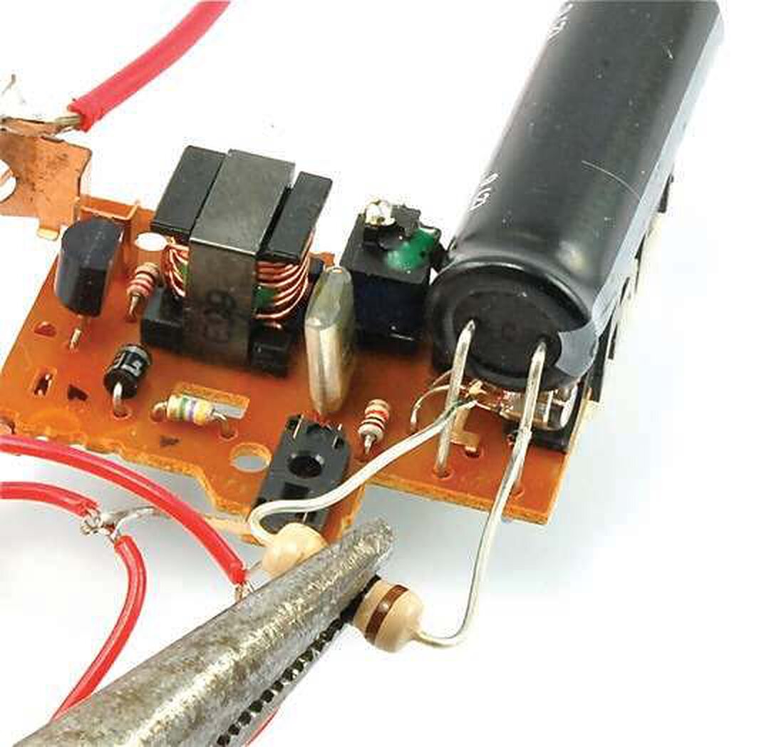 A resistor held in the teeth of pliers pressed across the terminals of a large capacitor on a power-supply board