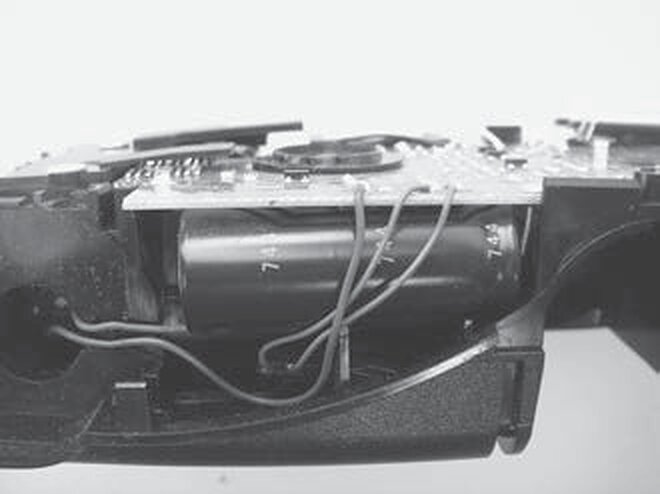 The inside of a film camera with the large cylindrical 330-volt strobe capacitor visible